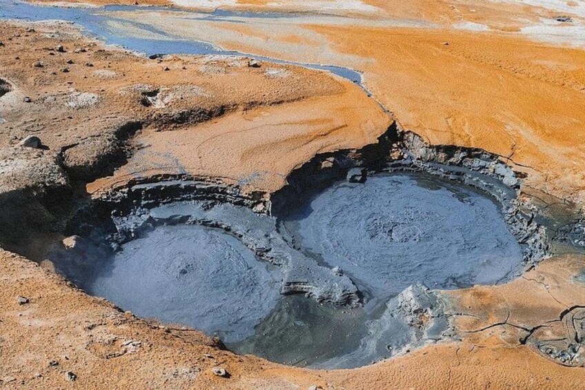 Une zone géothermique comprenant deux sources chaudes circulaires, entourées d’un paysage aux teintes rouge-brun. 3