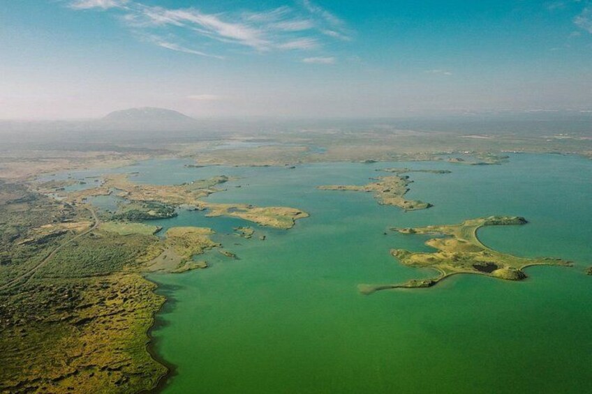 Vue aérienne d’une zone côtière avec une eau verdâtre, des étendues de terre et une montagne lointaine. 2