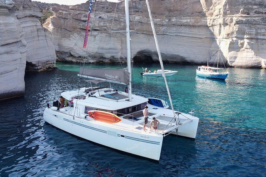 Un velero blanco con cabina y vela azul, amarrado cerca de formaciones rocosas blancas en un cuerpo de agua. 5