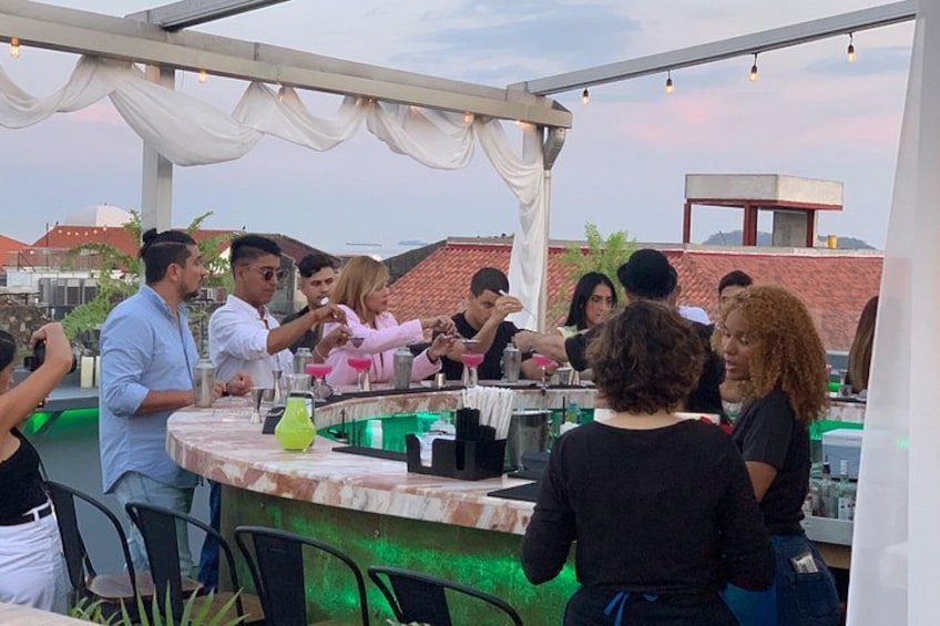 A group of people socializing at an outdoor bar with a white canopy, surrounded by chairs and tables. 5