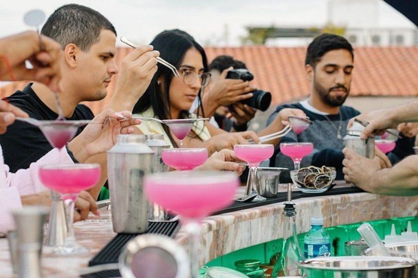 A group of people at a bar, some holding drinks and others taking photos. 1