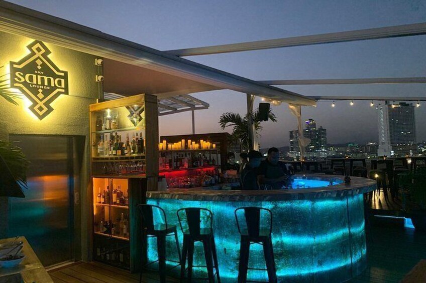 En bar på taket med en pool, ett barområde och stadens silhuett som bakgrund. 3