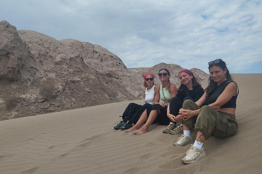 Four people sitting on a sand dune with a rocky landscape in the background. 2