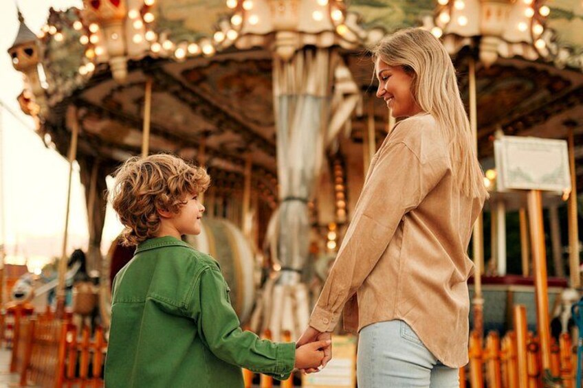 A carousel with lights and a person holding hands with a child. 1