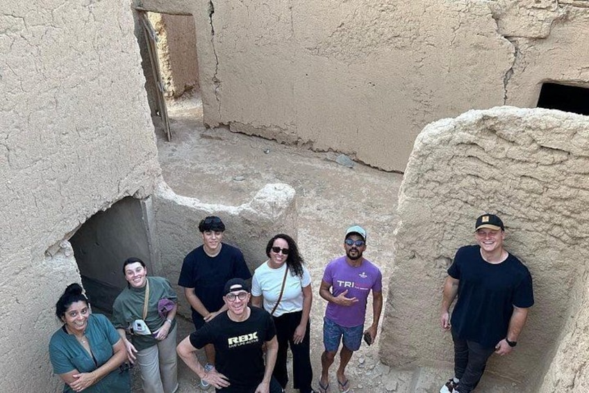 A group of people standing in an ancient, narrow alleyway with rough, textured walls and a small opening at the end. 4