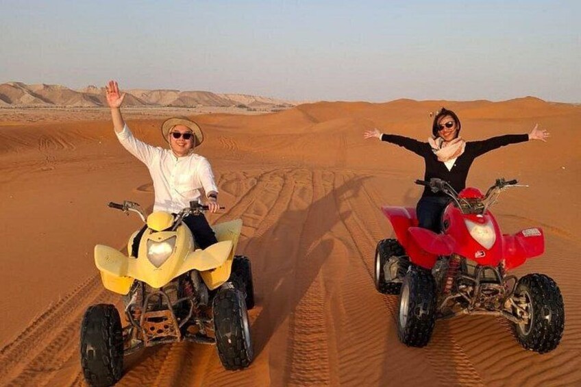 Two people on quad bikes in a desert with sand dunes in the background. 2
