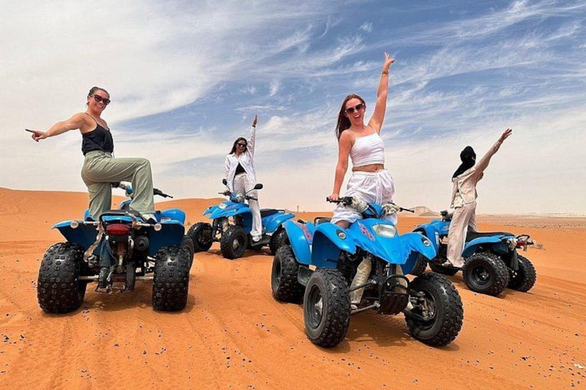 Four people on blue off-road vehicles in a desert with sand dunes. 1