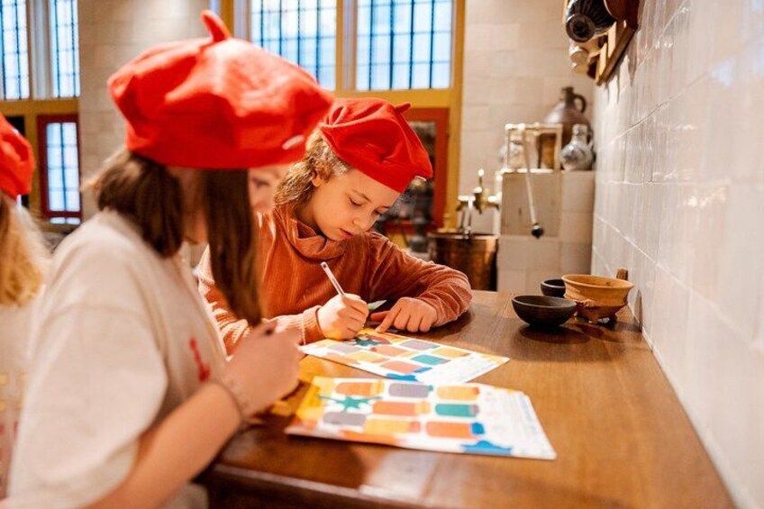 Une personne portant un béret rouge, assise à une table devant un dessin coloré. 1