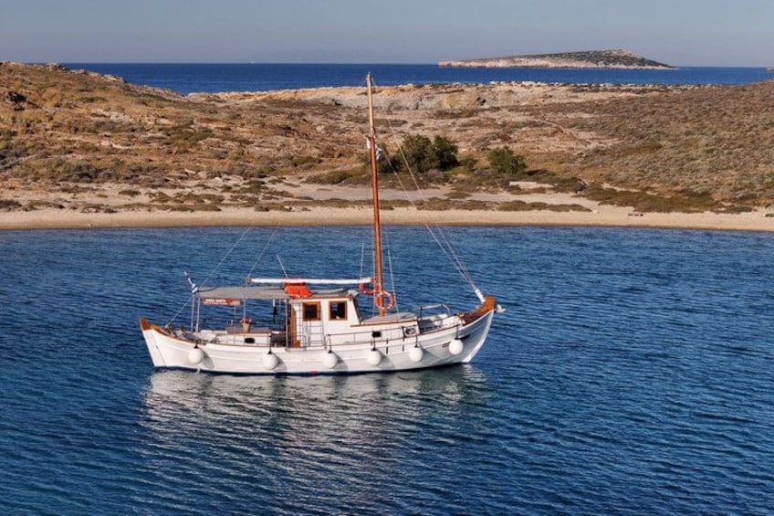 Een witte boot met een rode kajuit op kalm blauw water, omgeven door een rotsachtige kustlijn en een zandstrand. 2