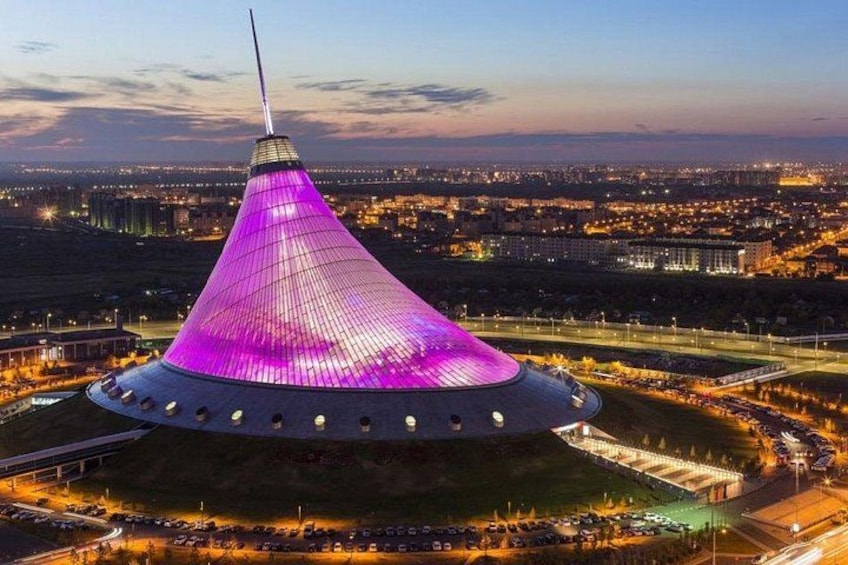 A large, conical building with a pointed top, surrounded by a parking lot and a cityscape in the background. 3