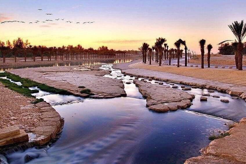 A river with water flowing through a concrete channel, surrounded by palm trees and a paved walkway. 3