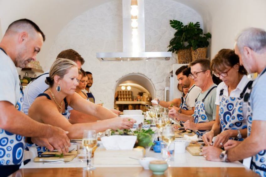 Eine Gruppe von Personen in Schürzen bereitet Essen an einem Tresen zu, im Hintergrund ist ein Backofen aus Ziegelsteinen zu sehen. 2