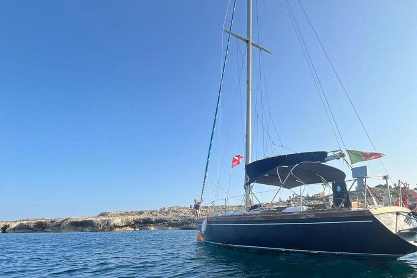 Een zeilboot op kalm water, met een heldere lucht en een rotsachtige kustlijn op de achtergrond. 1