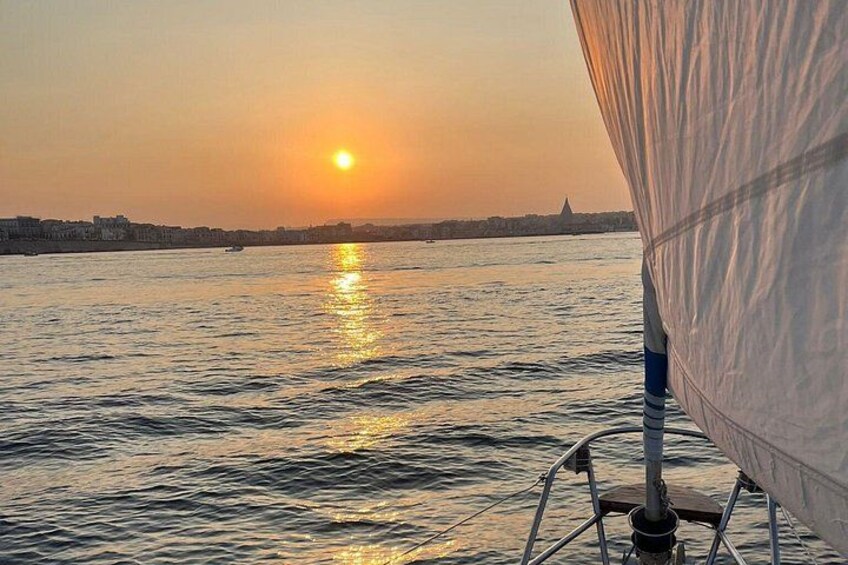 Een zonsondergang boven een wateroppervlak, met een zeilboot op de voorgrond. 2
