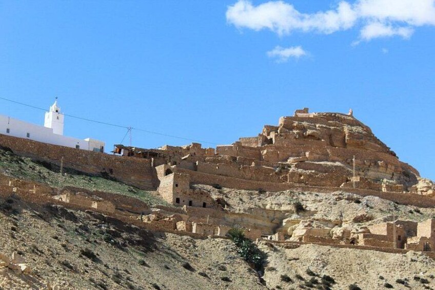 A historical site with ancient ruins and a white building with a bell tower. 3