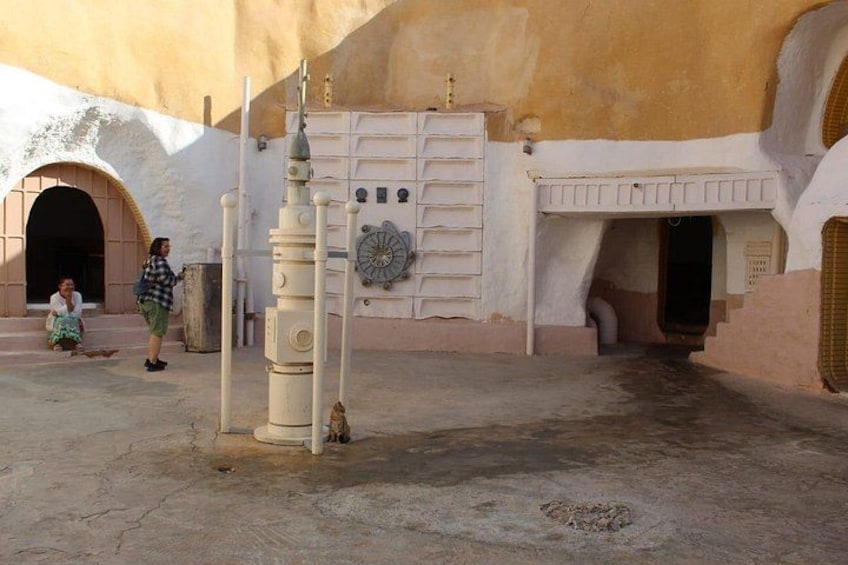 A desert landscape with a large, white, arched doorway and a small, white tower-like structure in the foreground. 1