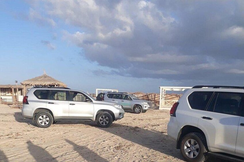 A sandy area with parked cars and a thatched-roof structure. 5
