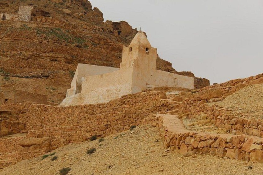A white building with a bell tower on a rocky hillside. 2