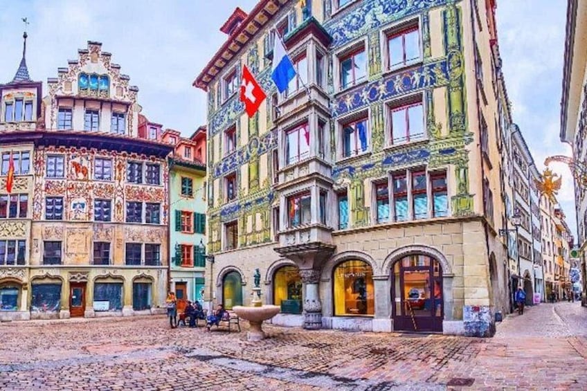 A cobblestone street with ornate buildings, flags, and a fountain. 2