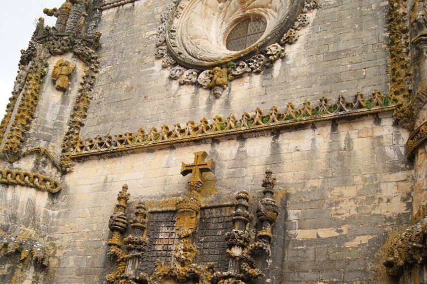 A historic building facade with ornate stone carvings, a large circular window, and a prominent cross. 1
