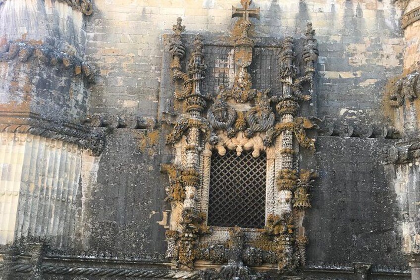 A weathered stone facade with intricate carvings and a central window with a lattice design. 5