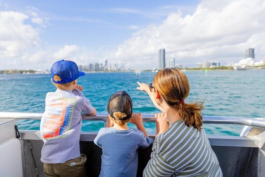 Three people on a boat, looking at a city skyline across the water. 3