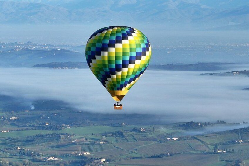 A hot air balloon with a checkered pattern flying over a landscape with fields and distant mountains. 5