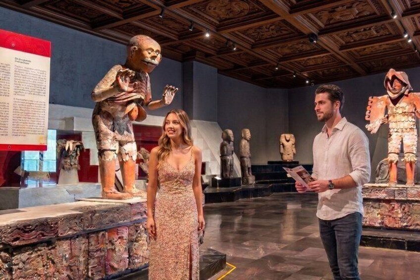 Een museuminterieur met oude beelden en een persoon die een brochure vasthoudt. 3
