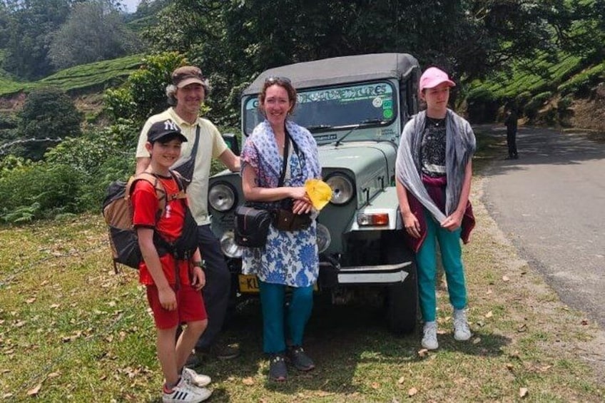 A group of people standing beside a green off-road vehicle in a grassy area with trees in the background. 2