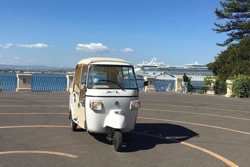 Un vehículo blanco de tres ruedas estacionado en un estacionamiento, con un crucero al fondo. 4
