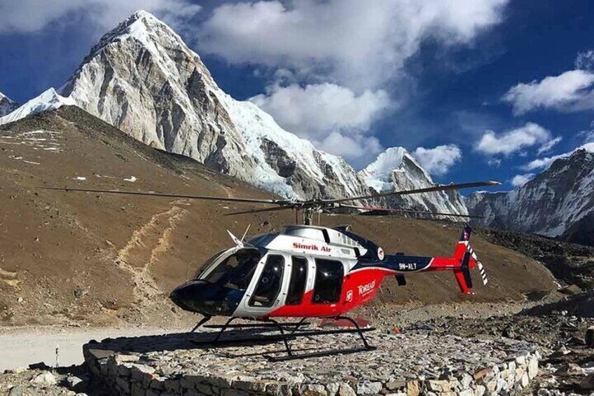 A helicopter parked on a rocky terrain with snow-capped mountains in the background. 4