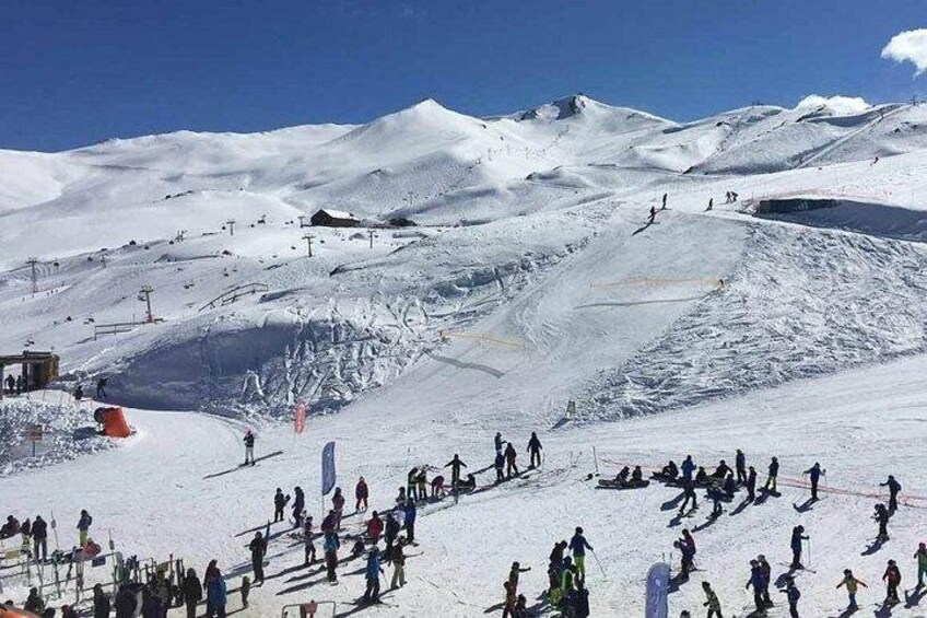 Une pente de montagne enneigée, avec des skieurs et des snowboardeurs, un tél ésiège et un ciel bleu dégagé. 1