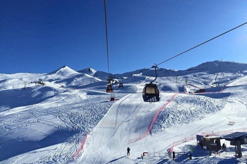 Un télésiège avec des câbles, une pente de montagne enneigée et un ciel bleu dégagé. 3