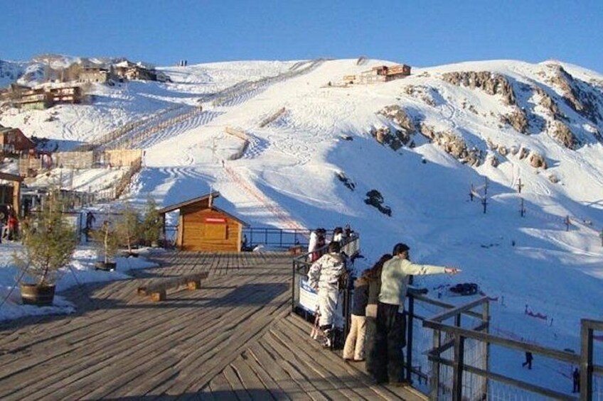 Une pente de montagne enneigée, avec une plateforme d’observation en bois, un petit bâtiment rouge et une personne qui pointe du doigt vers la pente. 5