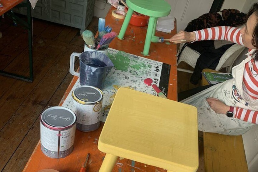 A person painting a wooden table with a yellow paintbrush. 1