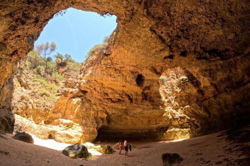 A large rock formation with a natural archway, a person standing in the foreground, and a clear blue sky visible through the opening. 1