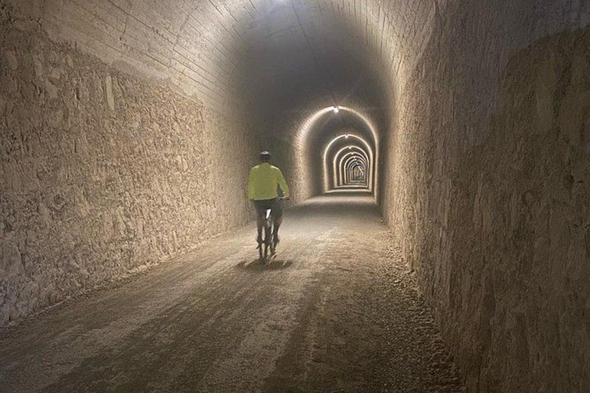 A cyclist riding through a tunnel with arched ceilings and a series of lights along the path. 4