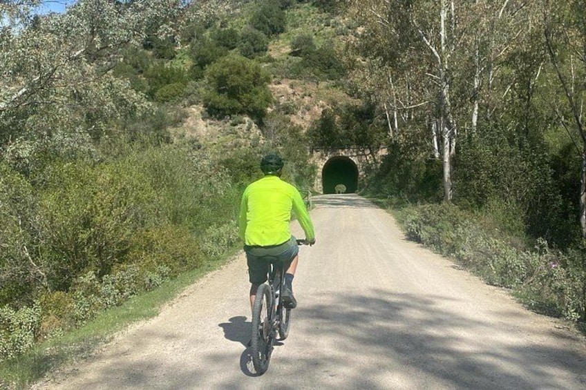 A person riding a bicycle on a dirt road with a tunnel in the distance. 2