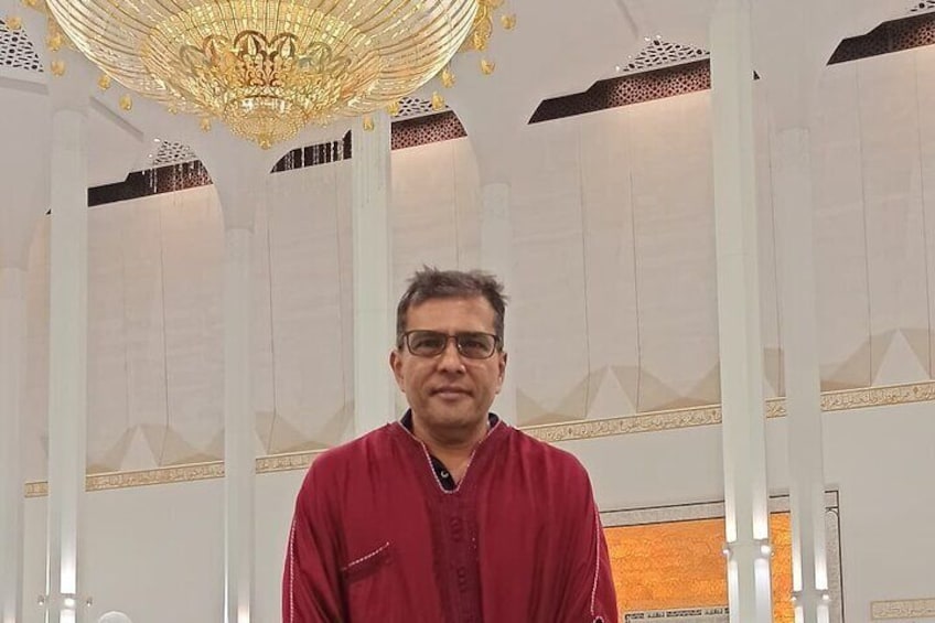A man in a red shirt standing in a room with white columns and a large chandelier. 4