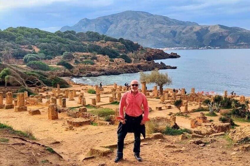 A person standing in front of ancient ruins with a coastal landscape in the background. 2