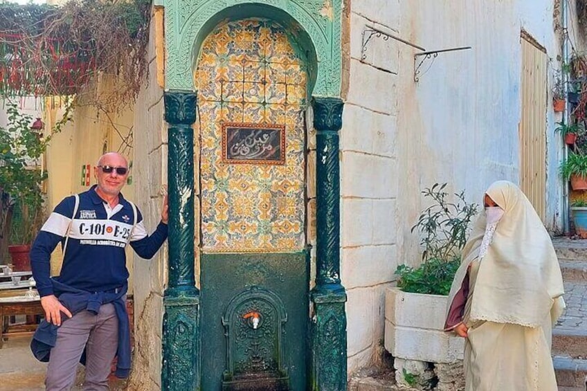 A man standing next to a building with a decorative entrance and a woman in traditional attire walking by. 1