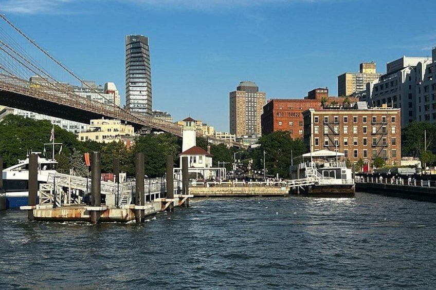 Eine Stadtansicht am Wasser mit einer Brücke, einem hohen Gebäude und einem historischen Bauwerk. 2