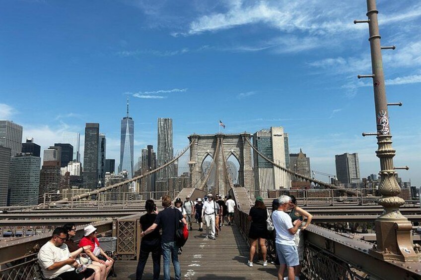 A bridge with people walking and sitting, overlooking a city skyline with tall buildings. 3