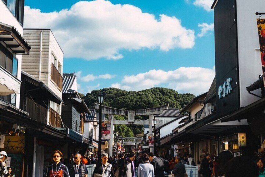 A busy street with people walking, traditional buildings, and a hill in the background. 1