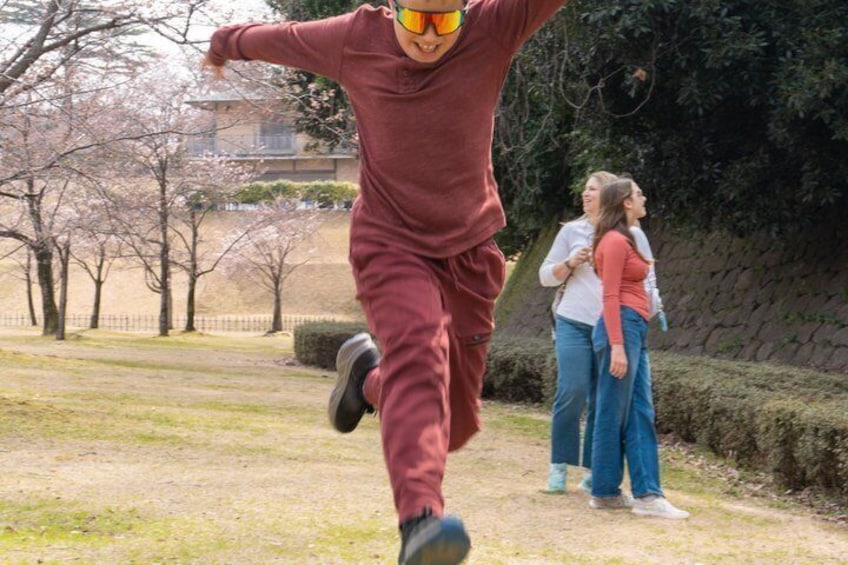 A person in a red outfit jumping in a park with cherry blossoms and a stone wall in the background. 5