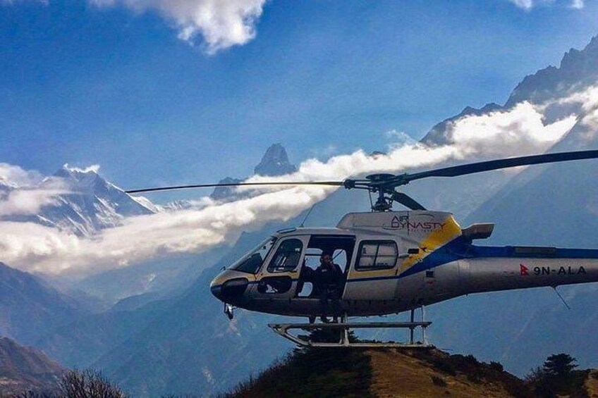 A helicopter with the registration B9N-ALA flying over a mountainous landscape with snow-capped peaks and clouds below. 2