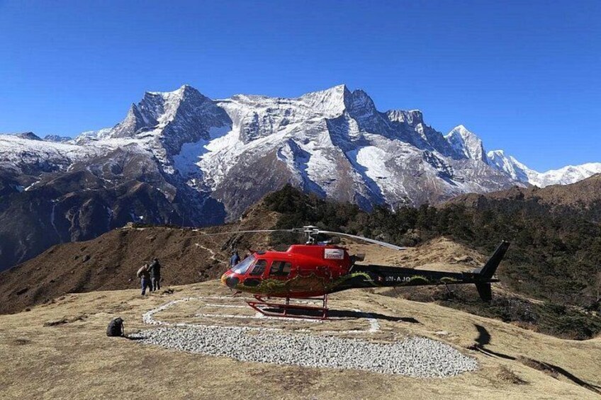 A red helicopter parked on a gravel surface with a mountainous backdrop. 1