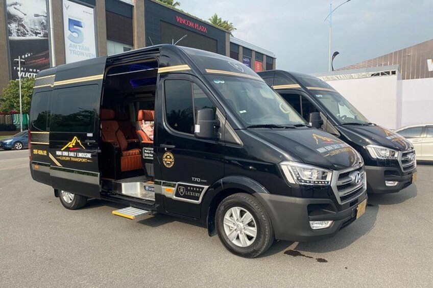 A black van with an open door, a logo on the side, and a building with a sign in the background. 3