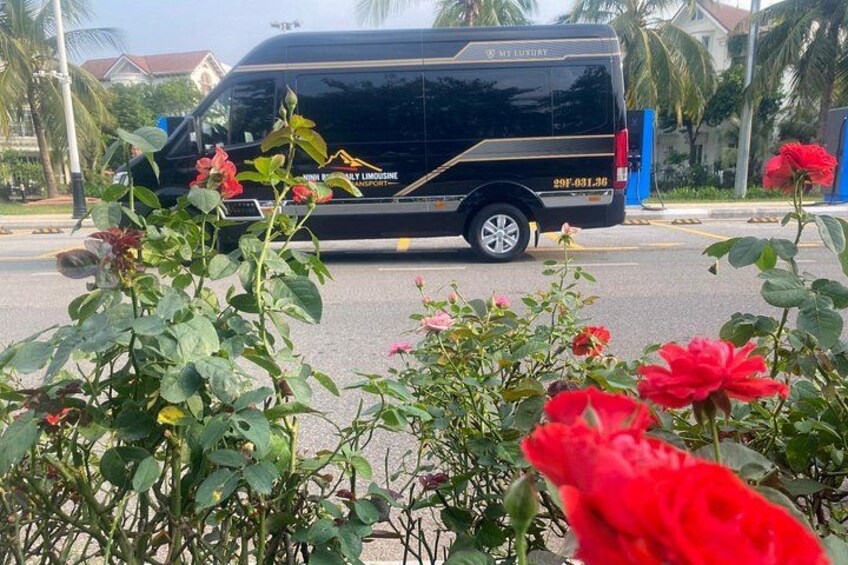 A black van with a floral design and a phone number on the side, parked on a street with red flowers in the foreground. 2