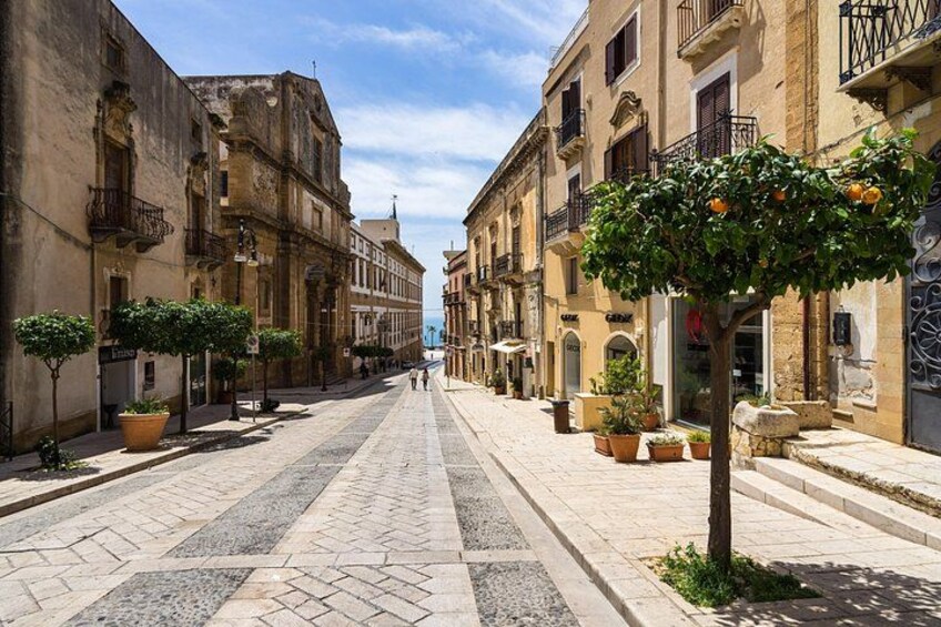 A cobblestone street lined with historic buildings, potted plants, and a clear blue sky. 4